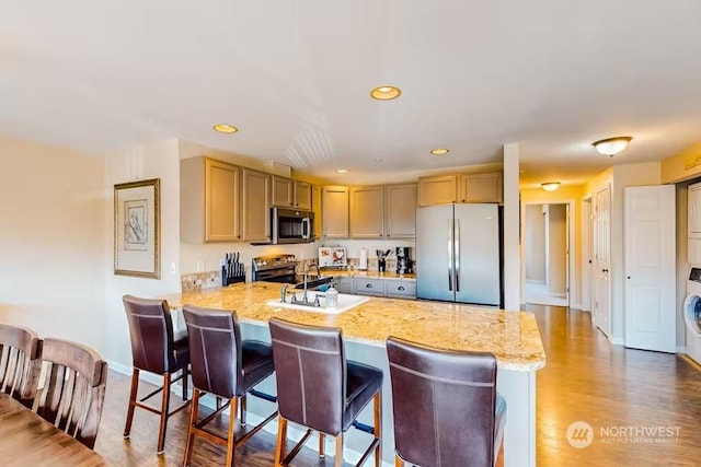 kitchen featuring light brown cabinets, sink, light hardwood / wood-style flooring, appliances with stainless steel finishes, and kitchen peninsula