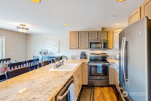 kitchen with appliances with stainless steel finishes, light brown cabinetry, sink, dark hardwood / wood-style floors, and a breakfast bar area