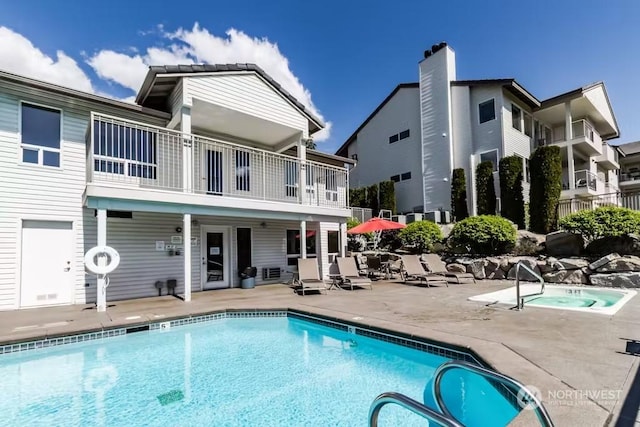 back of property with a swimming pool with hot tub, a balcony, and a patio