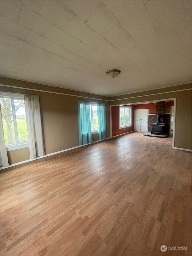 unfurnished living room with a healthy amount of sunlight, a wood stove, and light hardwood / wood-style flooring