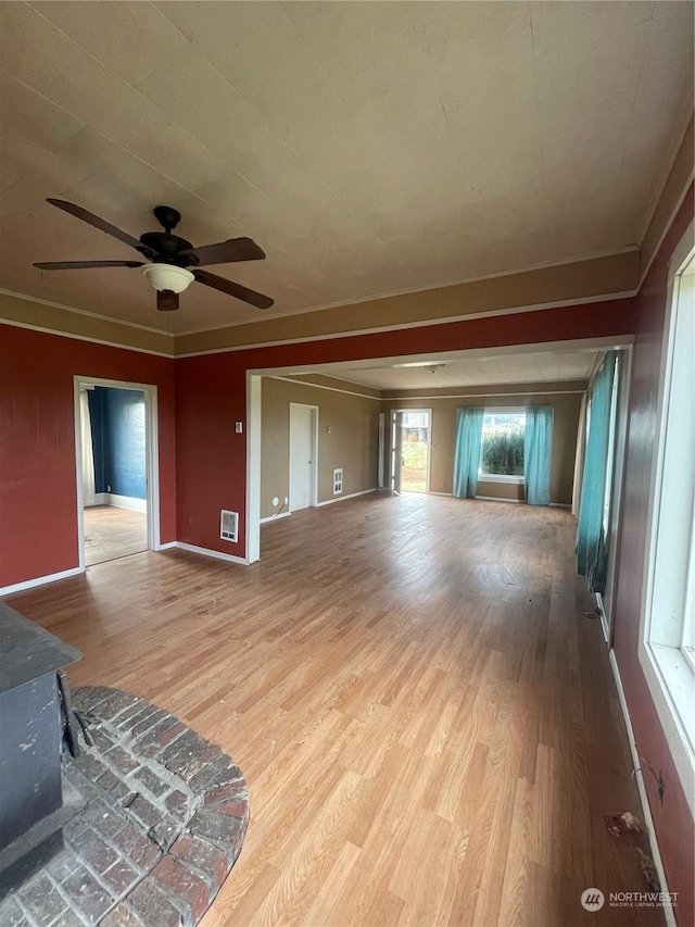 unfurnished living room featuring light hardwood / wood-style floors, ceiling fan, and a wood stove