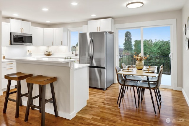 kitchen with a kitchen island, white cabinets, light wood-type flooring, and appliances with stainless steel finishes