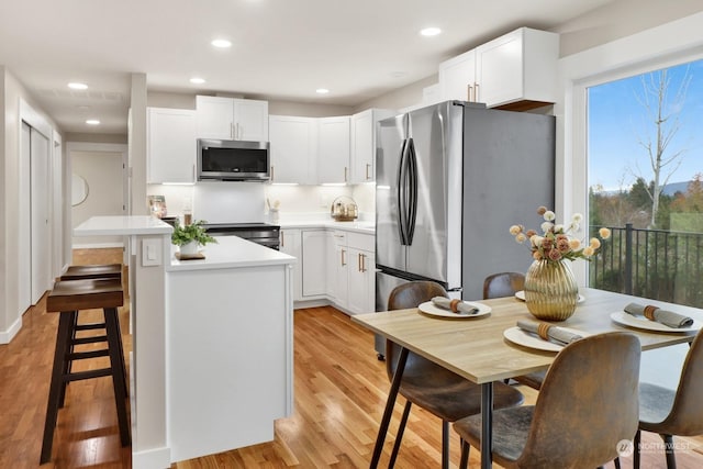 kitchen with light hardwood / wood-style flooring, appliances with stainless steel finishes, a kitchen island, white cabinetry, and a breakfast bar area