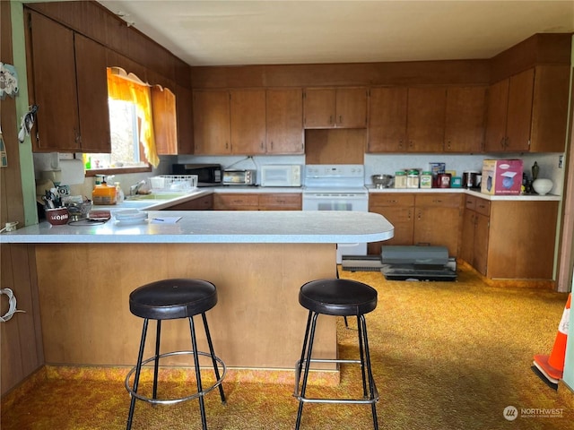 kitchen with kitchen peninsula, white appliances, a breakfast bar area, and sink