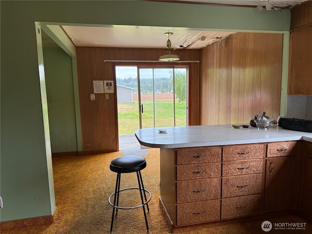 2978 Alexson Rd, North Cove, WA 98547 - kitchen featuring a peninsula, wood walls, light countertops, carpet flooring, and brown cabinets