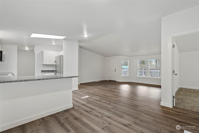 unfurnished living room with dark wood-type flooring and vaulted ceiling with skylight