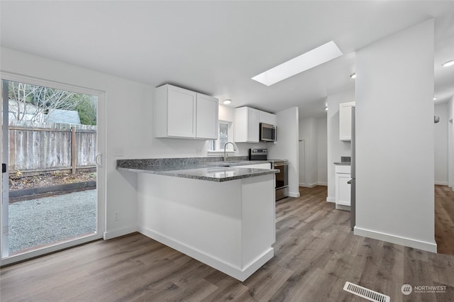 kitchen with appliances with stainless steel finishes, a skylight, sink, wood-type flooring, and white cabinetry