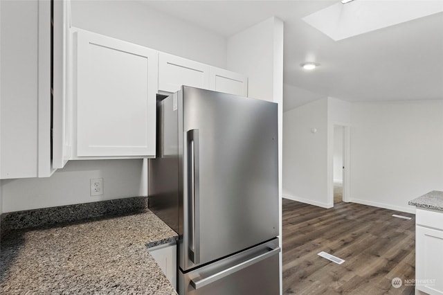 kitchen featuring stainless steel refrigerator, white cabinetry, a skylight, dark wood-type flooring, and stone countertops