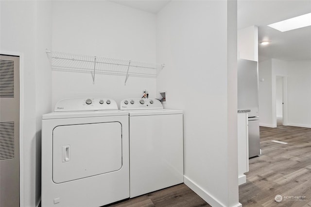 laundry area with wood-type flooring, a skylight, and washer and clothes dryer