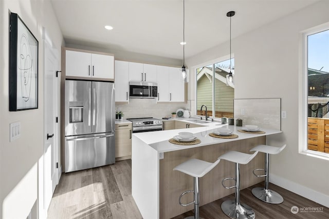 kitchen with kitchen peninsula, white cabinetry, stainless steel appliances, and decorative light fixtures