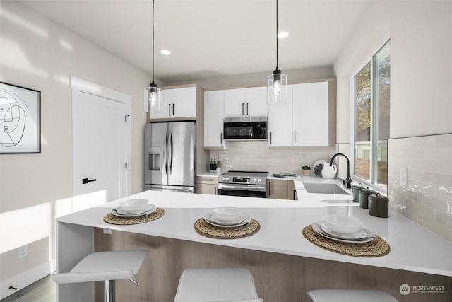 kitchen featuring appliances with stainless steel finishes, decorative light fixtures, white cabinetry, and plenty of natural light