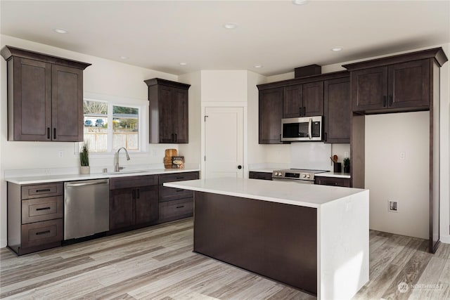 kitchen with sink, dark brown cabinets, stainless steel appliances, light hardwood / wood-style floors, and a kitchen island