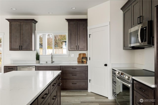 kitchen with dark brown cabinetry, sink, light hardwood / wood-style flooring, and appliances with stainless steel finishes