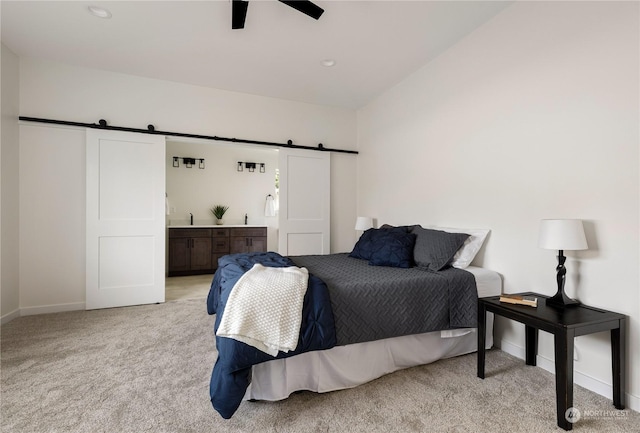 carpeted bedroom with a barn door, ceiling fan, and ensuite bathroom