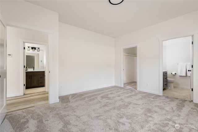 unfurnished bedroom featuring connected bathroom, a spacious closet, light colored carpet, and sink