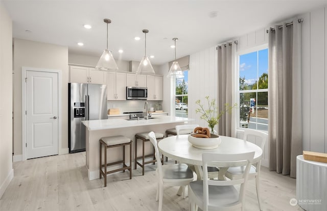 kitchen featuring white cabinets, a center island with sink, hanging light fixtures, appliances with stainless steel finishes, and light hardwood / wood-style floors