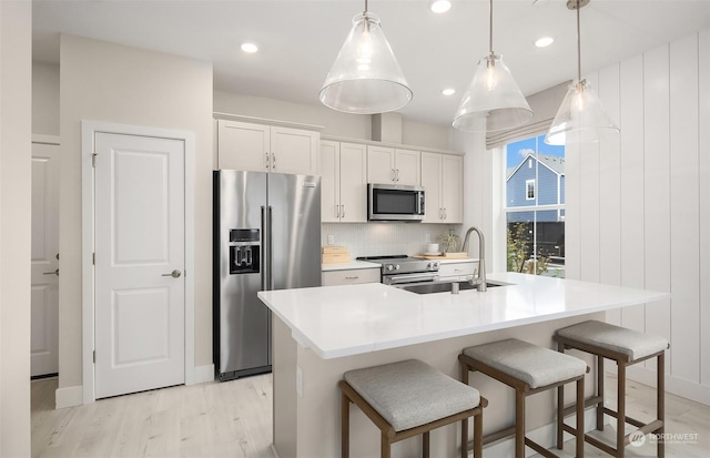 kitchen featuring appliances with stainless steel finishes, decorative light fixtures, white cabinetry, and an island with sink