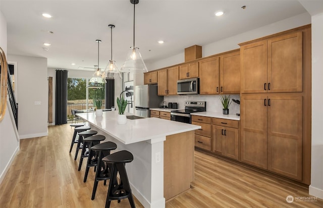 kitchen featuring appliances with stainless steel finishes, light wood-type flooring, a breakfast bar, decorative light fixtures, and an island with sink