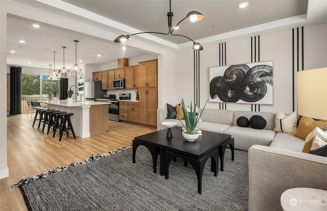 living room featuring a chandelier, a raised ceiling, light hardwood / wood-style flooring, and sink