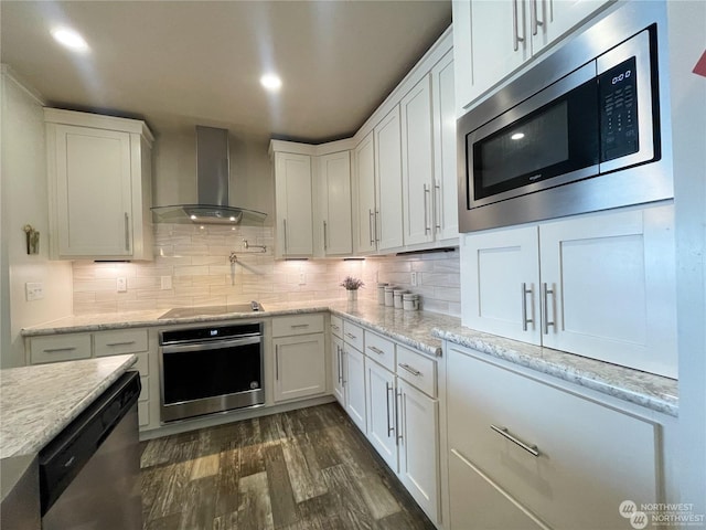 kitchen with wall chimney exhaust hood, decorative backsplash, appliances with stainless steel finishes, dark hardwood / wood-style flooring, and white cabinetry