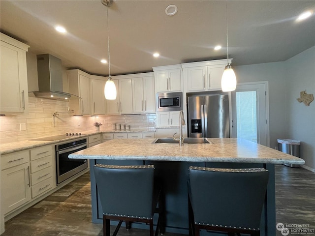 kitchen featuring stainless steel appliances, wall chimney exhaust hood, and an island with sink