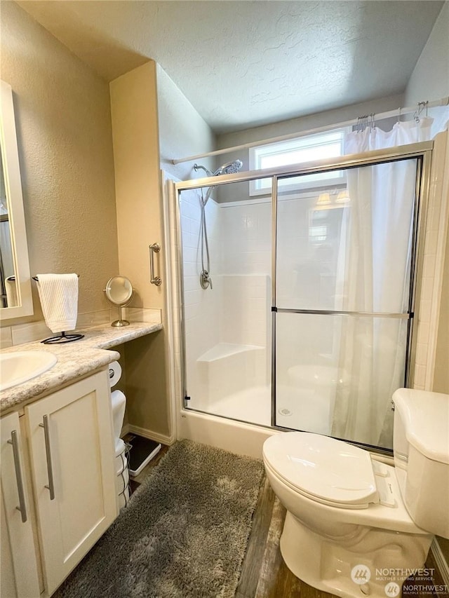 bathroom with hardwood / wood-style floors, vanity, toilet, a textured ceiling, and a shower with shower door