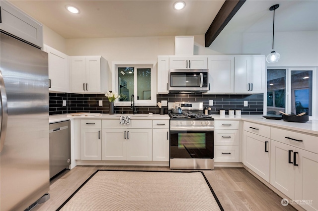 kitchen featuring tasteful backsplash, hanging light fixtures, white cabinets, and stainless steel appliances