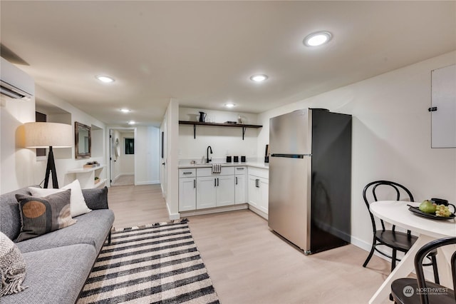 interior space featuring stainless steel fridge, a wall unit AC, sink, light hardwood / wood-style floors, and white cabinetry