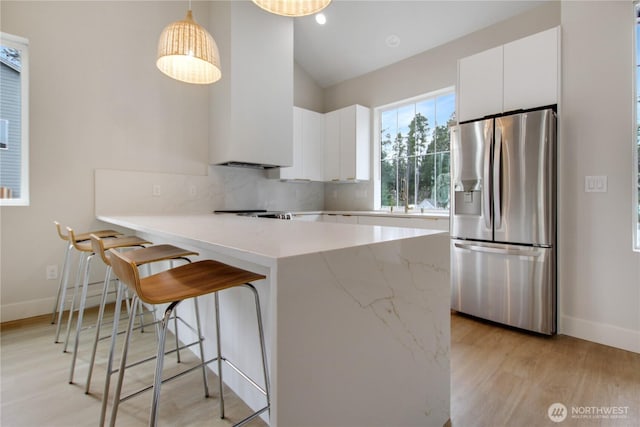 kitchen with light wood-type flooring, a peninsula, lofted ceiling, white cabinetry, and stainless steel fridge