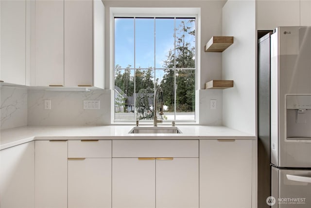 kitchen with open shelves, a sink, decorative backsplash, white cabinets, and stainless steel refrigerator with ice dispenser