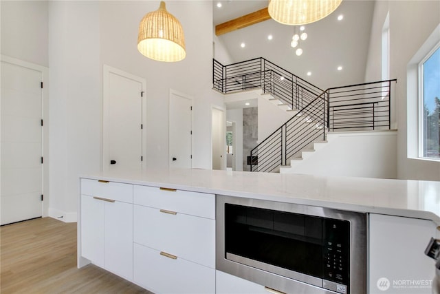 kitchen featuring light wood finished floors, a towering ceiling, white cabinetry, stainless steel microwave, and modern cabinets