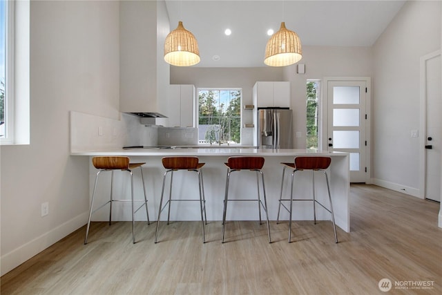 kitchen featuring stainless steel refrigerator with ice dispenser, a kitchen breakfast bar, a peninsula, white cabinets, and light countertops