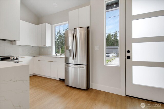 kitchen with a sink, white cabinets, appliances with stainless steel finishes, light wood-type flooring, and backsplash