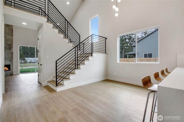 stairway featuring wood finished floors, baseboards, a high ceiling, recessed lighting, and a tiled fireplace