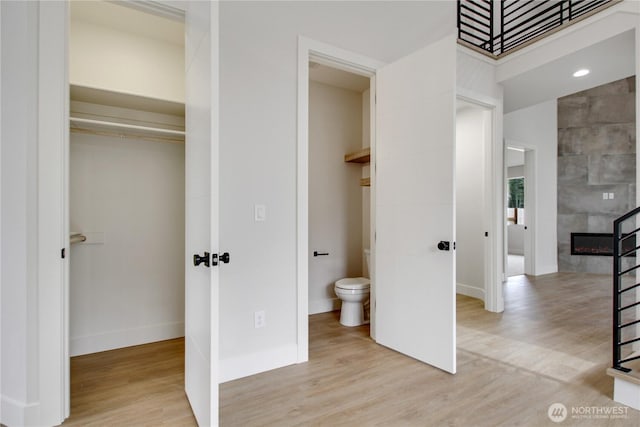 bathroom with a fireplace, toilet, baseboards, and wood finished floors