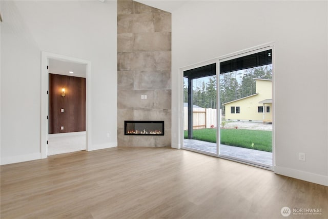 unfurnished living room with a fireplace, a high ceiling, baseboards, and wood finished floors