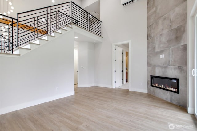 unfurnished living room with a tiled fireplace, stairway, a towering ceiling, and wood finished floors