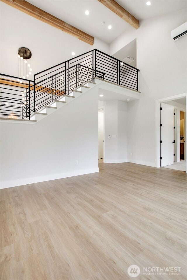 staircase featuring a wall unit AC, beamed ceiling, wood finished floors, and a high ceiling