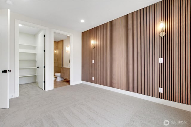 unfurnished bedroom with a closet, wood walls, a walk in closet, carpet flooring, and connected bathroom