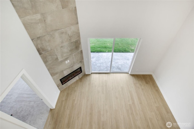 unfurnished living room featuring a tiled fireplace, baseboards, and wood finished floors