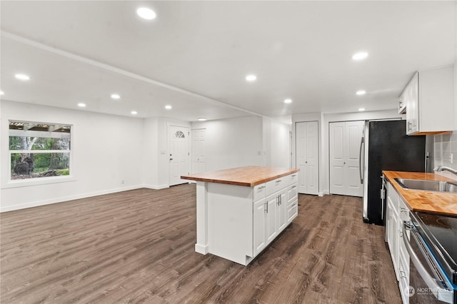 kitchen with dark wood-type flooring, sink, butcher block countertops, a kitchen island, and white cabinetry