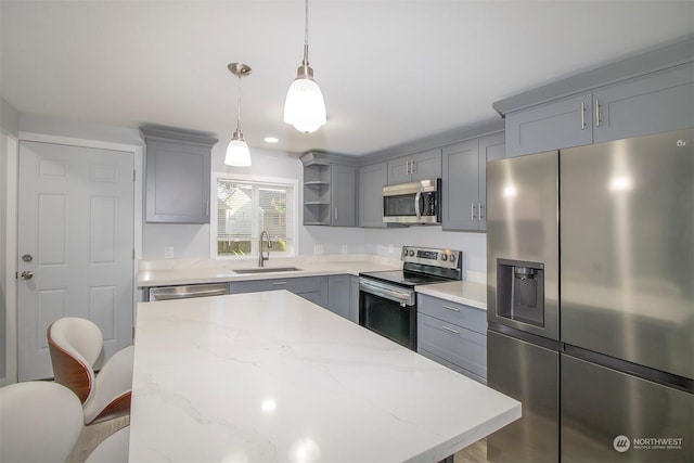 kitchen with gray cabinetry, sink, hanging light fixtures, a breakfast bar area, and stainless steel appliances