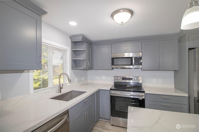 kitchen with light stone countertops, sink, decorative light fixtures, gray cabinets, and appliances with stainless steel finishes