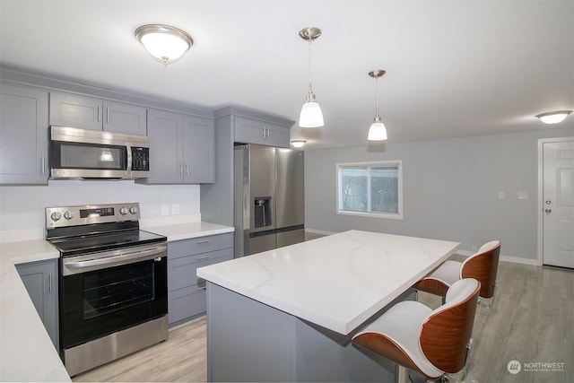 kitchen featuring stainless steel appliances, light hardwood / wood-style flooring, decorative light fixtures, gray cabinets, and a kitchen island