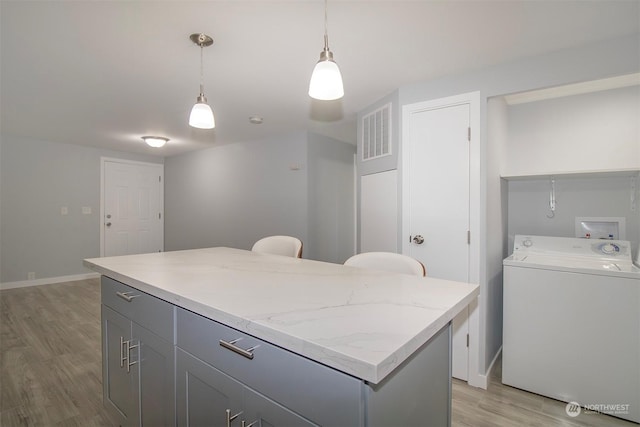 kitchen featuring washer / dryer, decorative light fixtures, light hardwood / wood-style flooring, and gray cabinetry