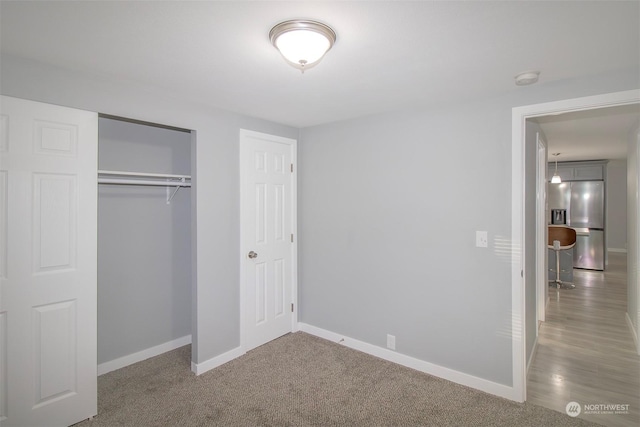 unfurnished bedroom featuring carpet flooring, stainless steel fridge, and a closet