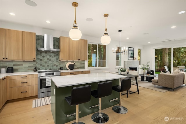 kitchen with wall chimney range hood, stainless steel stove, a kitchen island, plenty of natural light, and light hardwood / wood-style floors