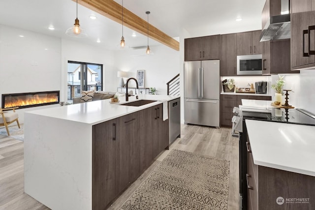 kitchen with sink, wall chimney exhaust hood, beamed ceiling, light hardwood / wood-style floors, and appliances with stainless steel finishes