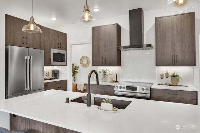 kitchen with a breakfast bar, wall chimney range hood, appliances with stainless steel finishes, decorative light fixtures, and dark brown cabinets