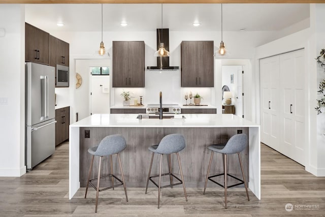 205 Riverwalk Dr, Lynden, WA 98264 - kitchen with stainless steel appliances, wall chimney exhaust hood, a kitchen bar, dark brown cabinetry, and light countertops